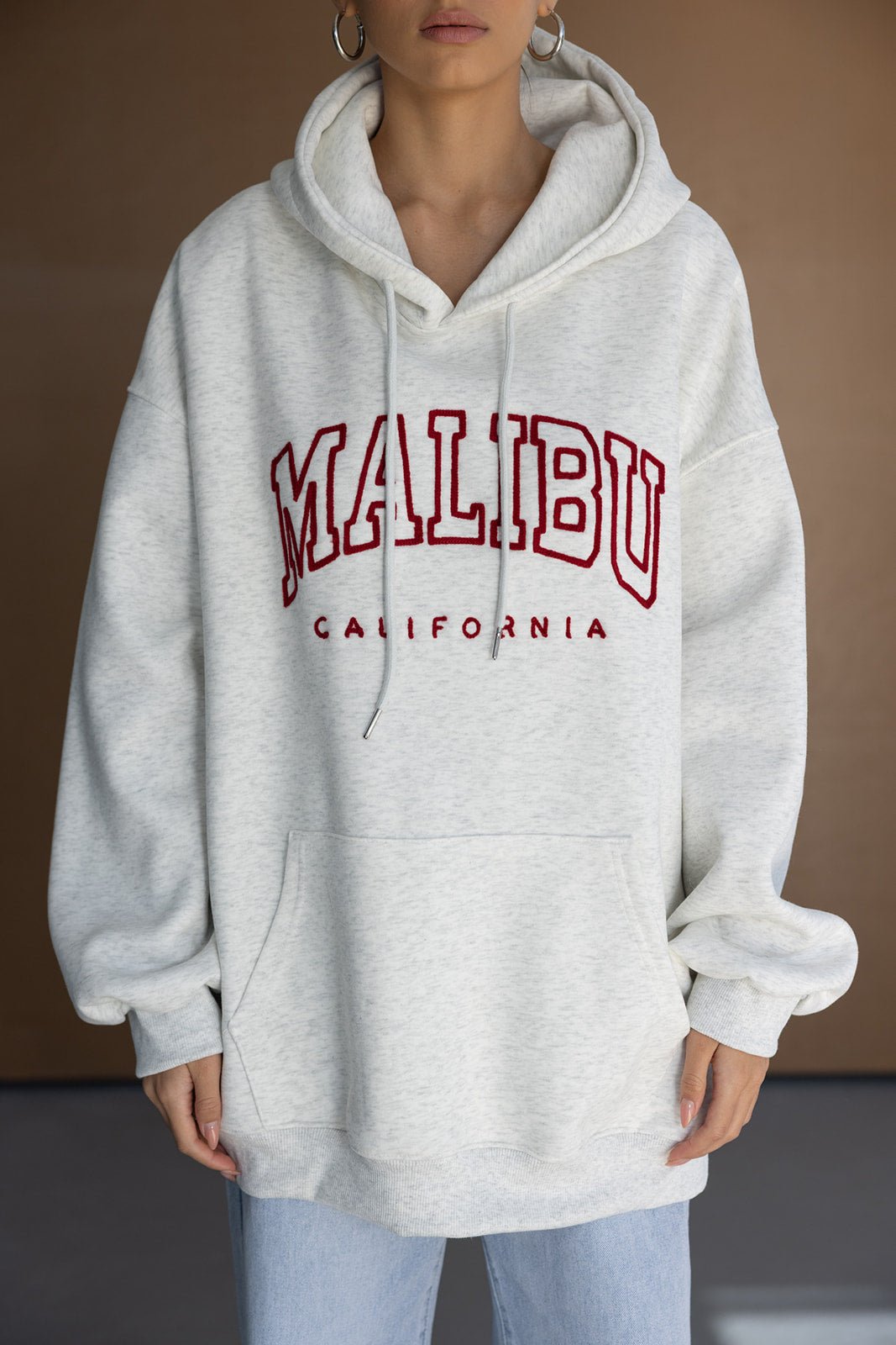 אישה לובשת קפוצ'ון אופנתי לבן עם כיתוב MALIBU אדום, מראה יומיומי לנשים צעירות