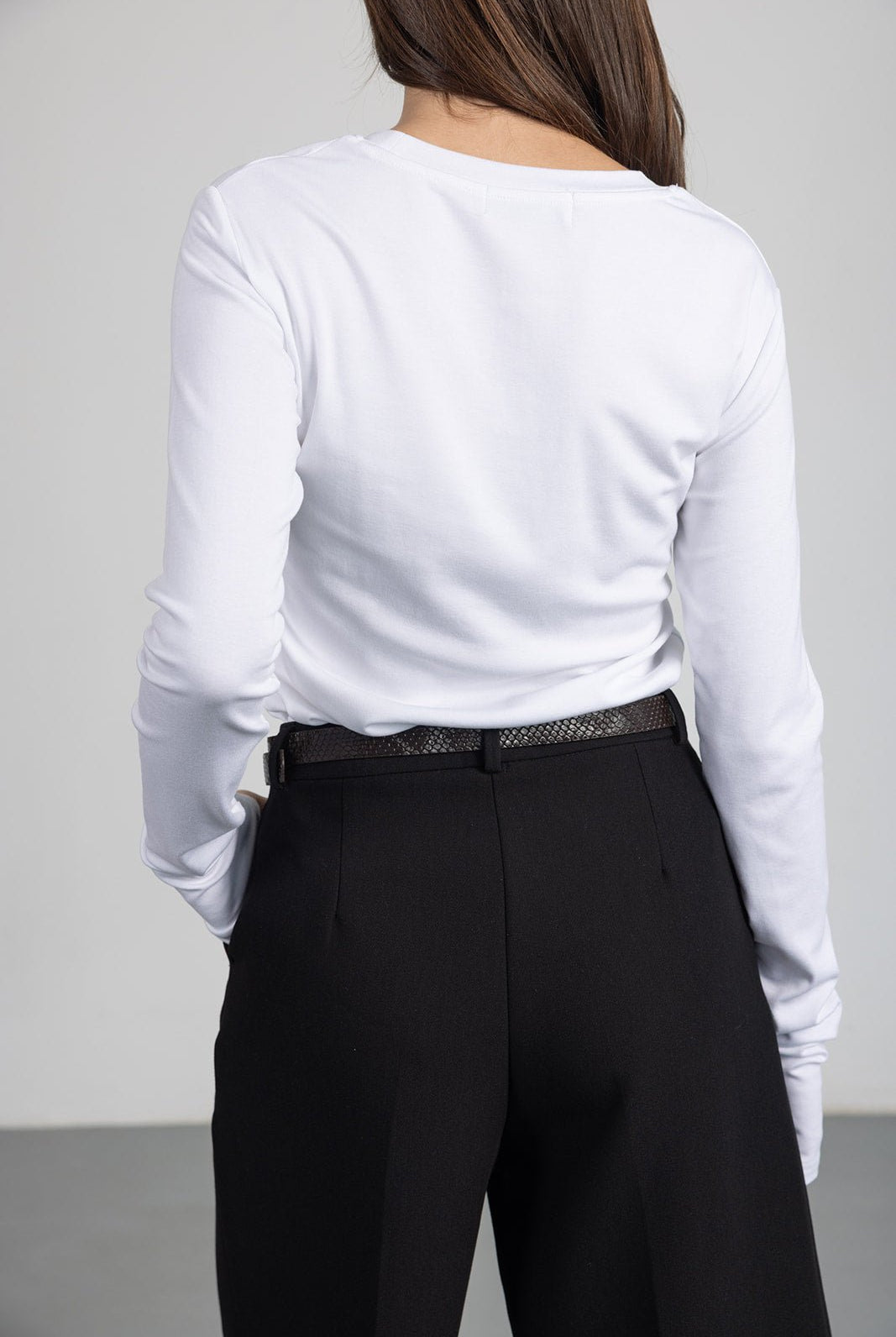 גברת לובשת חולצה לבנה עם שרוול ארוך ומכנסיים שחורים מחויטים, מבט מאחור, אופנה לנשים