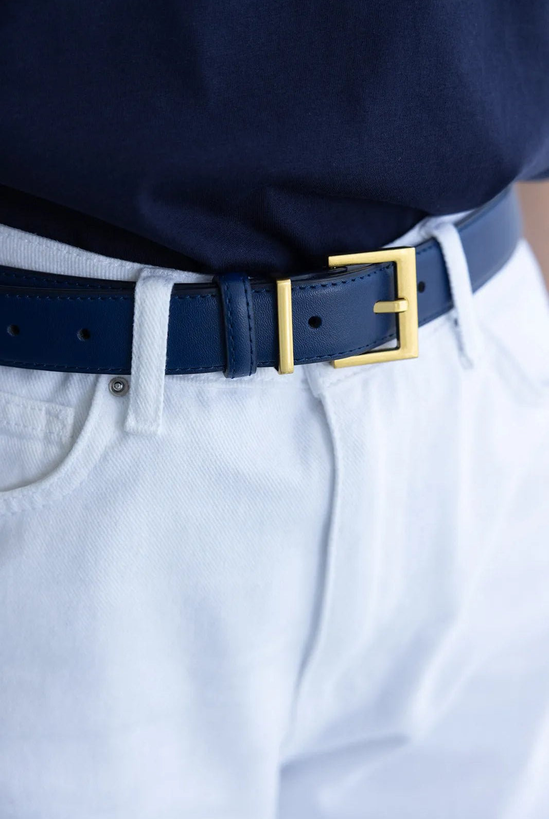 חגורת עור כחולה עם אבזם זהב על מכנסי ג'ינס לבנים, אופנת נשים צעירה