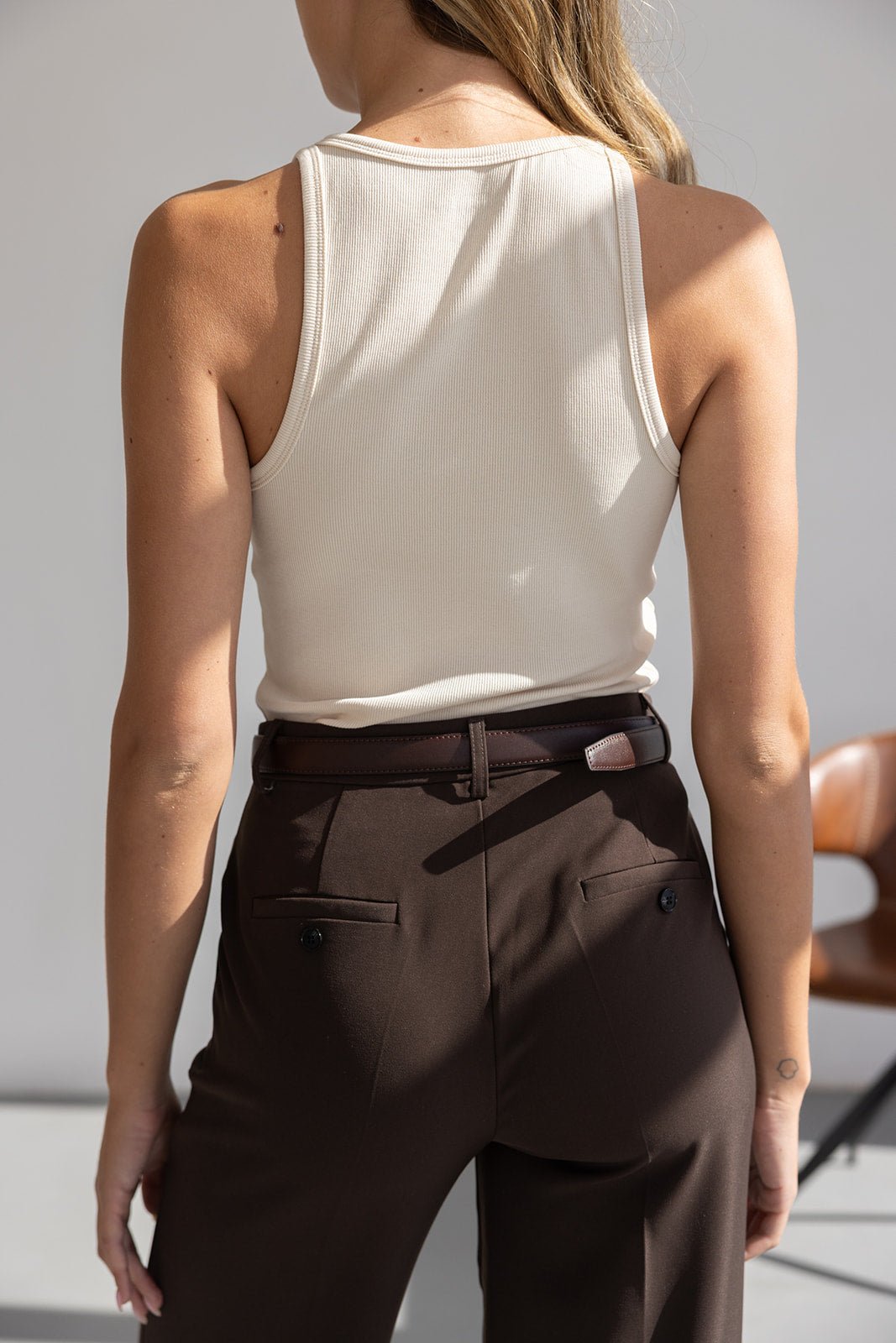 גב אישה עם גופיית סריג לבנה ומכנסי בד חומים, אופנה לנשים צעירות