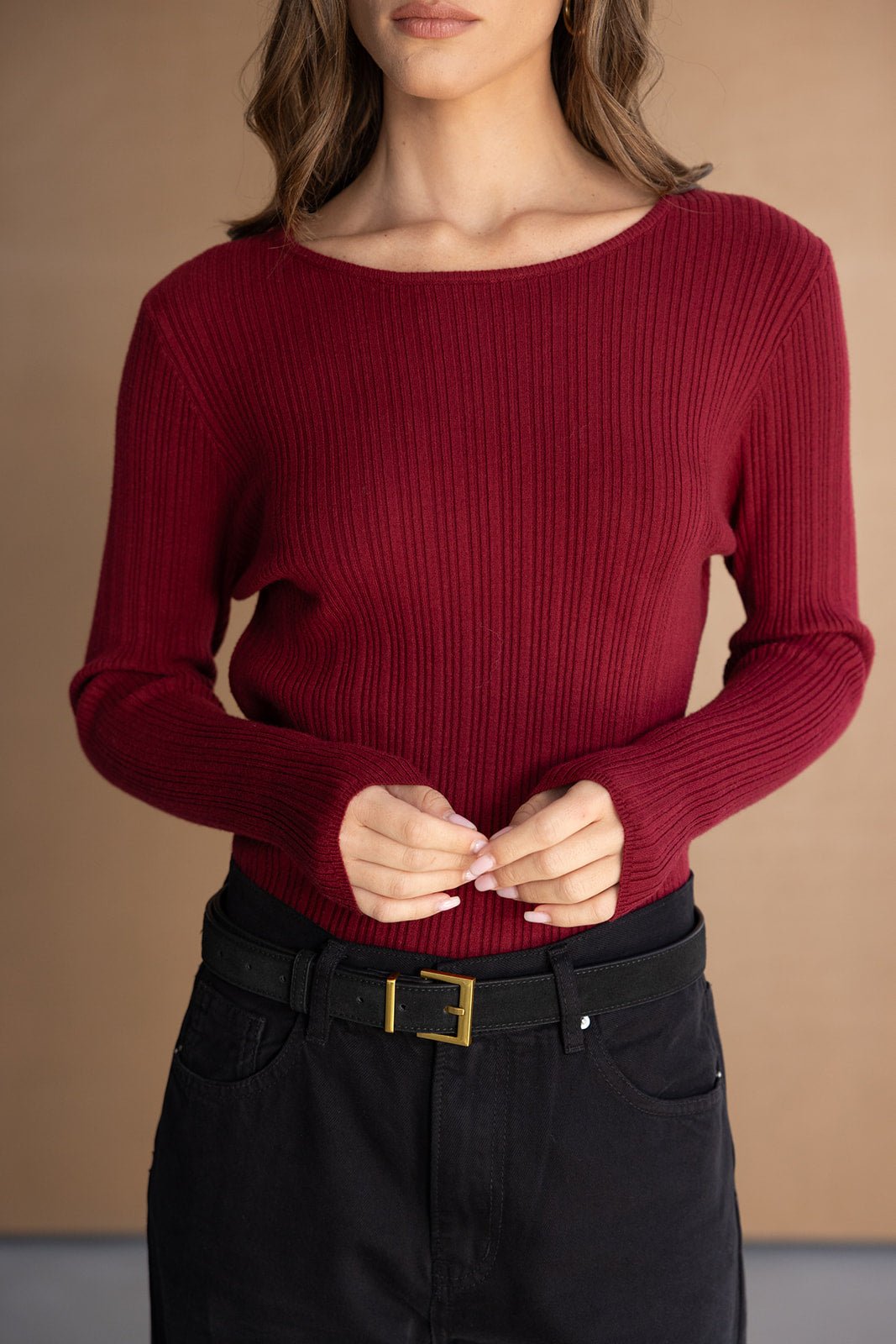 חולצת סריג אדום לנשים עם שרוולים ארוכים, משולבת במכנסי ג'ינס שחורים וחגורה שחורה