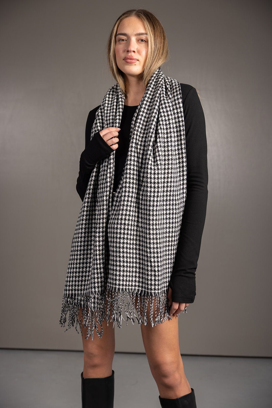 דוגמנית לובשת צעיף משובץ בשחור ולבן עם פרנזים, חולצה שחורה ומגפיים, אופנת חורף לנשים