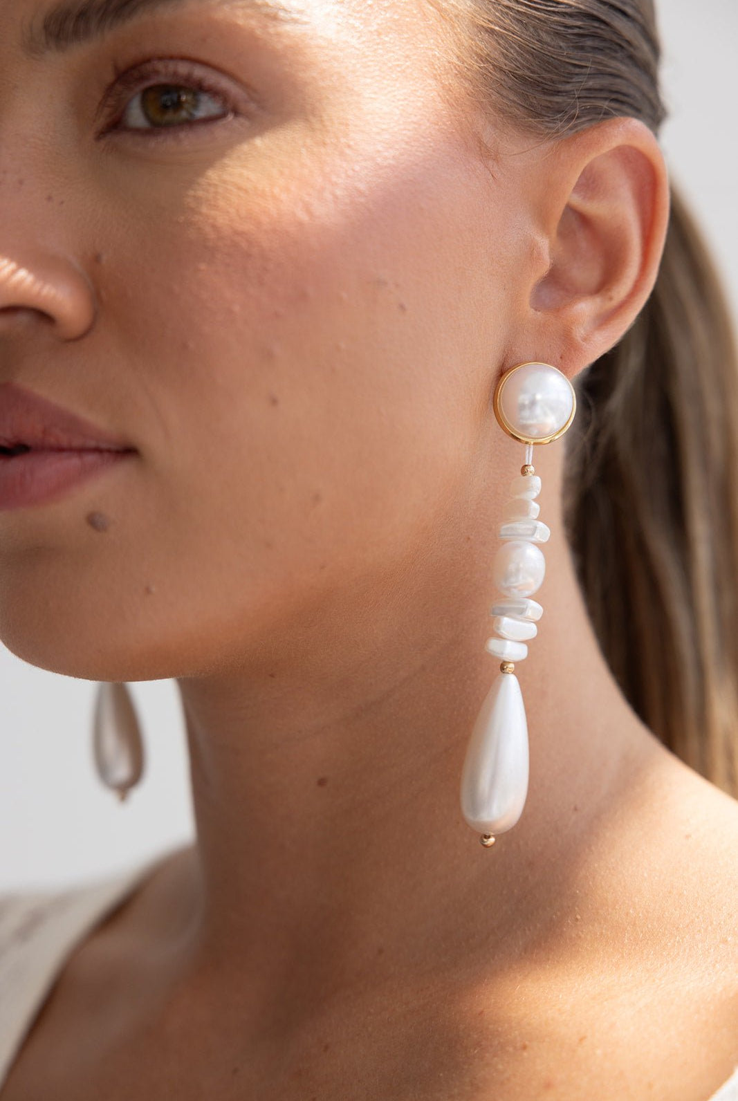 עגילי פנינה תלויים לנשים, עיצוב אלגנטי בגוון לבן וזהב, צילום תקריב על דוגמנית