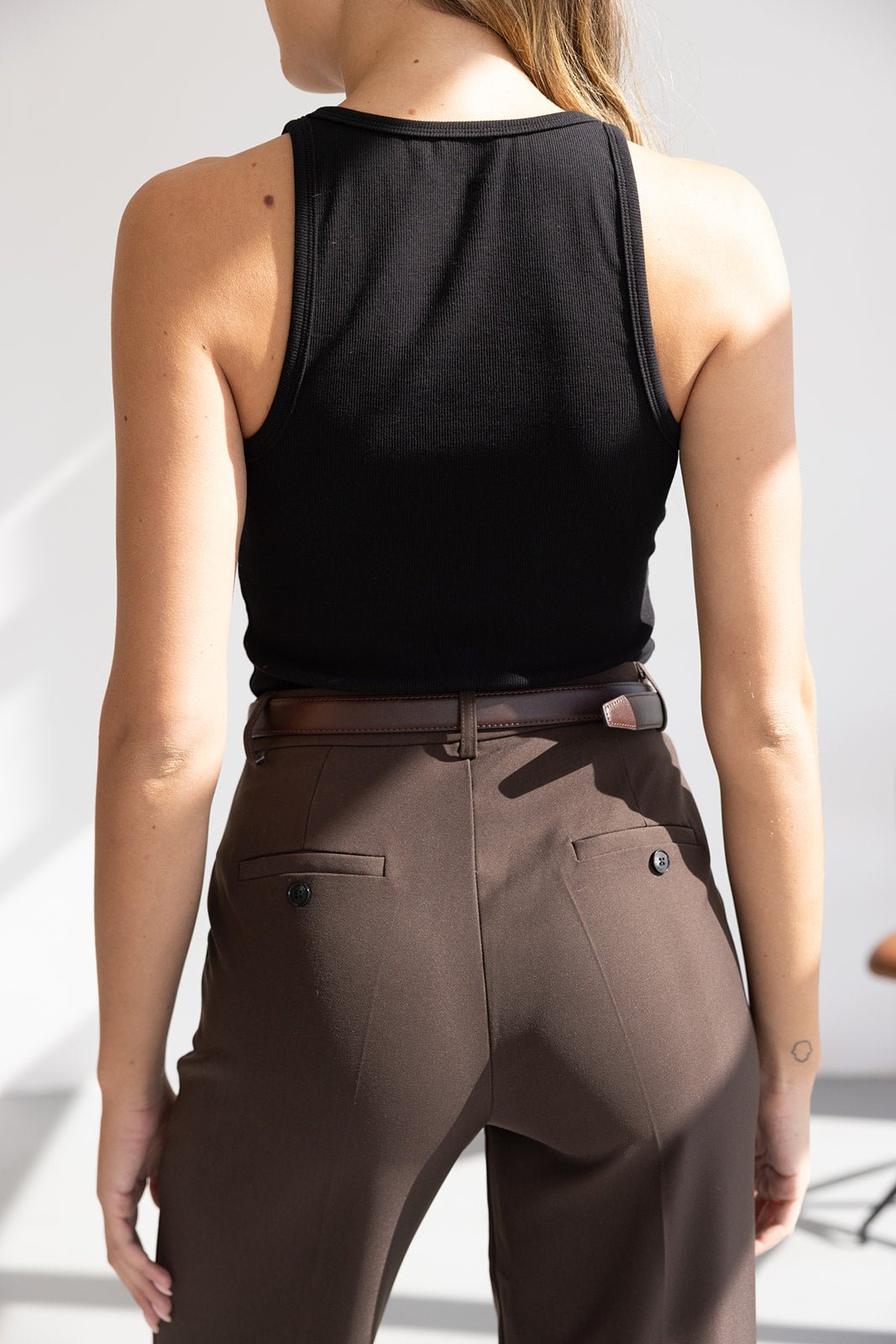 אישה עם גופיה שחורה ומכנסיים חומים אלגנטיים, מבט מאחור, אופנת נשים צעירה