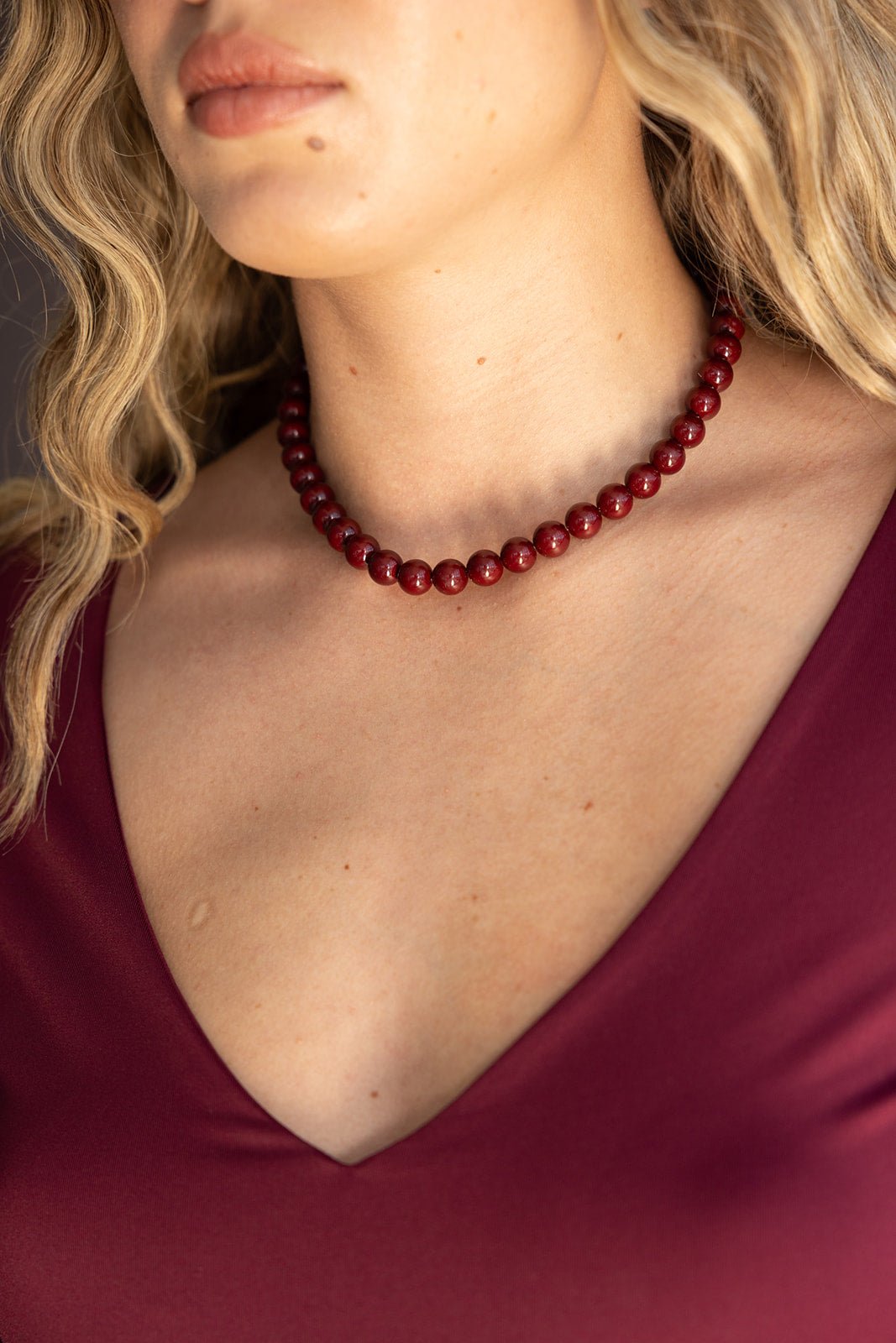 שרשרת חרוזים עגולים אדומים על אישה עם שמלת וי בורדו, אופנה לנשים