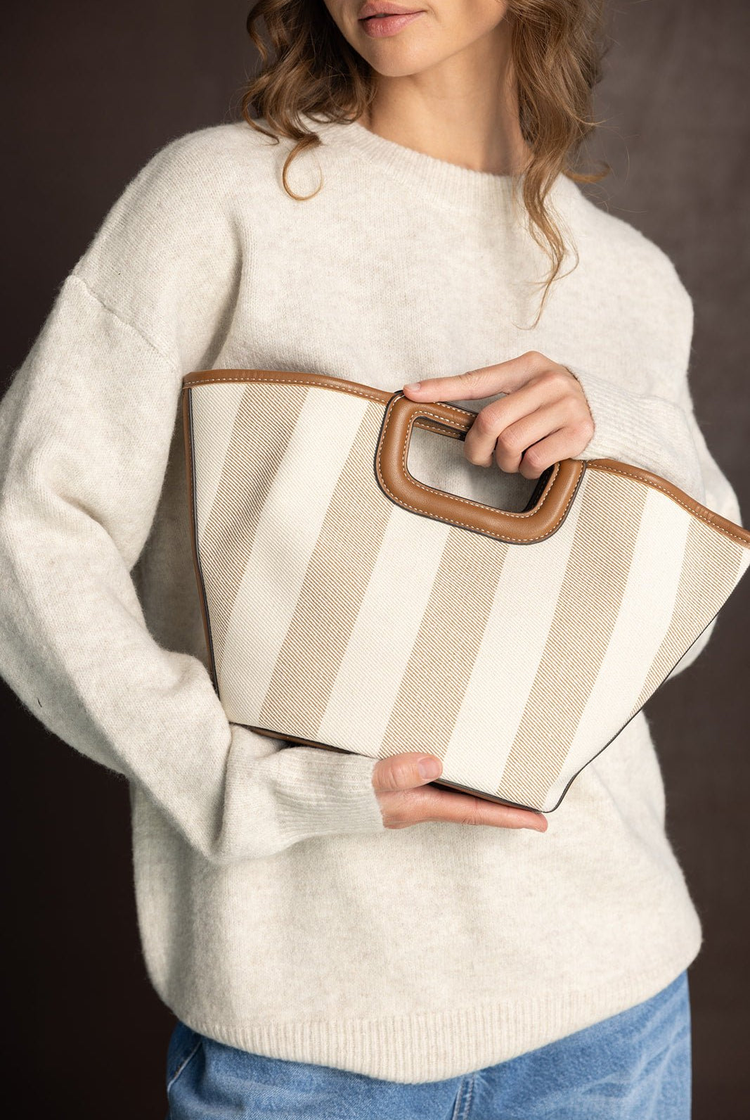 אישה עם סוודר בז' מחזיקה תיק יד בד פסים בז' ולבן, אופנה לנשים צעירות