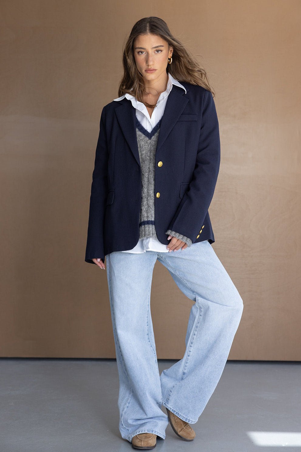 דוגמנית לובשת בלייזר כחול כהה, סוודר עם מפתח V, חולצה לבנה ומכנסי ג'ינס רחבים, לוק אופנתי לנשים