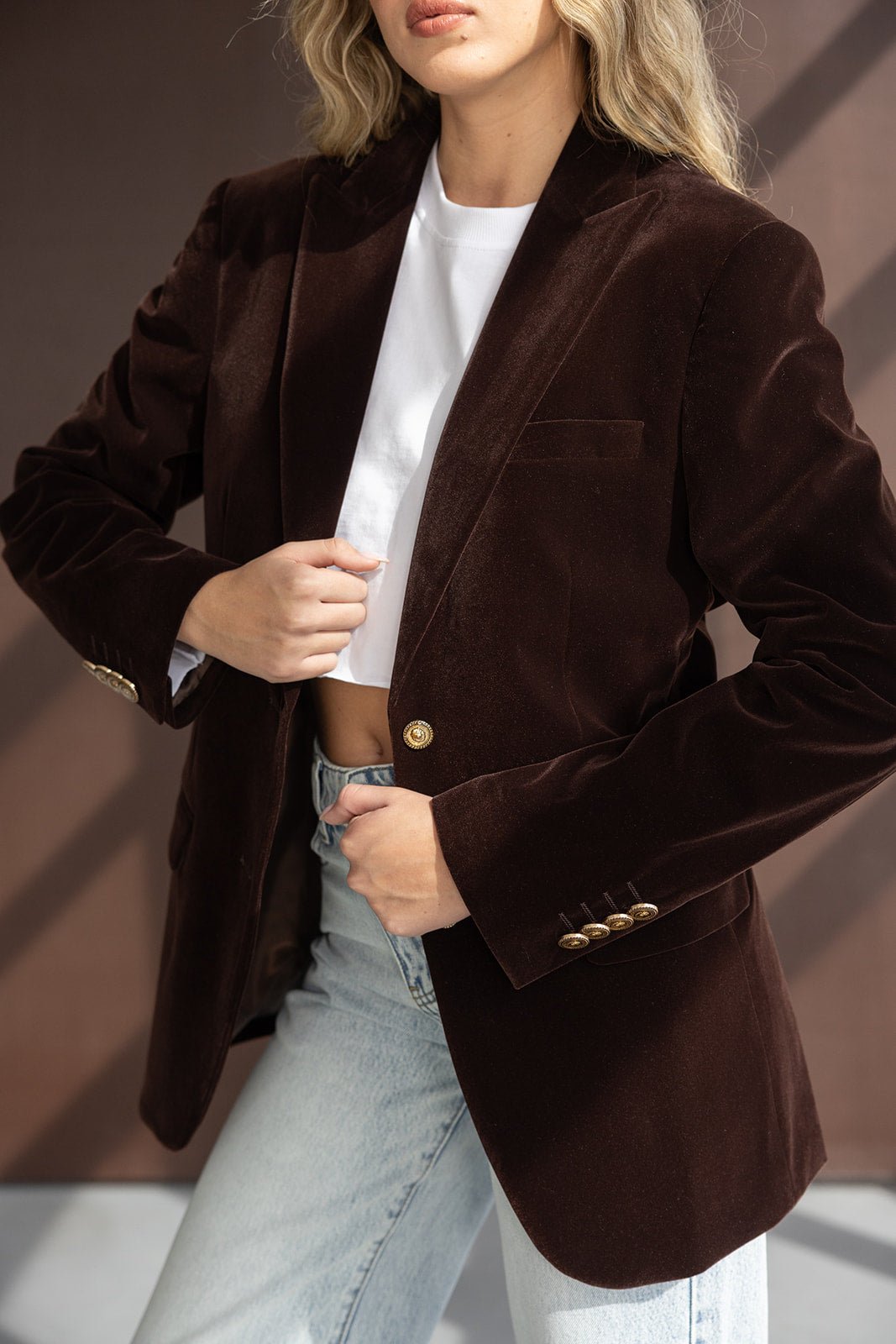 ז'קט קטיפה חום לאישה עם כפתורים זהב, חולצה לבנה וג'ינס בהיר – אופנת נשים טרנדית