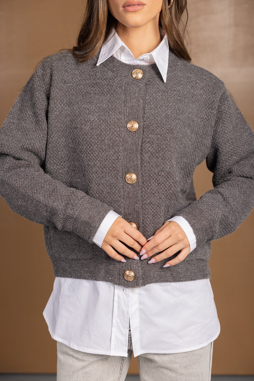 סריג נשים אפור עם כפתורים זהובים, חולצה לבנה מתחת, מראה אופנתי חורפי