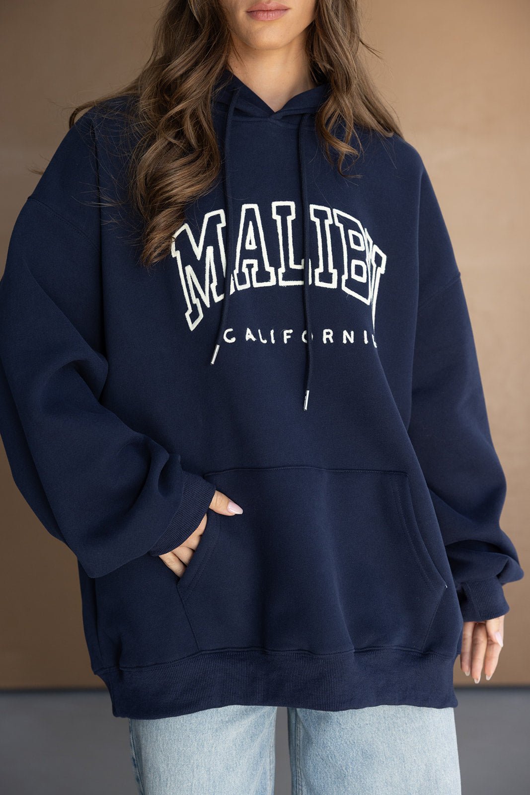 אישה עם קפוצ'ון כחול כהה עם כיתוב 'MALIBU CALIFORNIA', לוק קז'ואל אופנתי לנשים