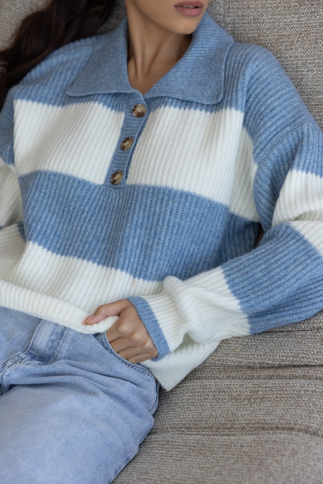 סוודר פסים כחול ולבן עם כפתורים גדולים, מונח על דוגמנית בלבוש קז'ואל, ישיבה על ספה