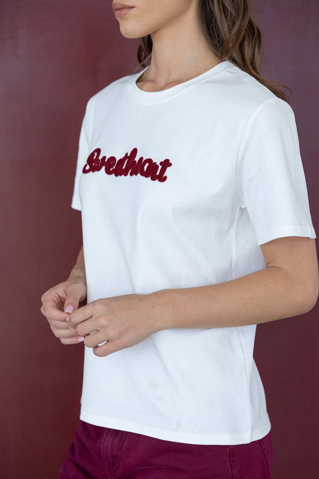 דוגמנית עם חולצת טי שירט לבנה כיתוב אדום ובגדי נשים אופנתיים, רקע בורדו