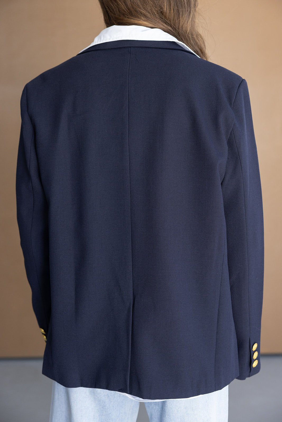 אישה לובשת בלייזר כחול עם צווארון לבן וכפתורים זהובים, צילום מגב, בגדי נשים אופנתיים