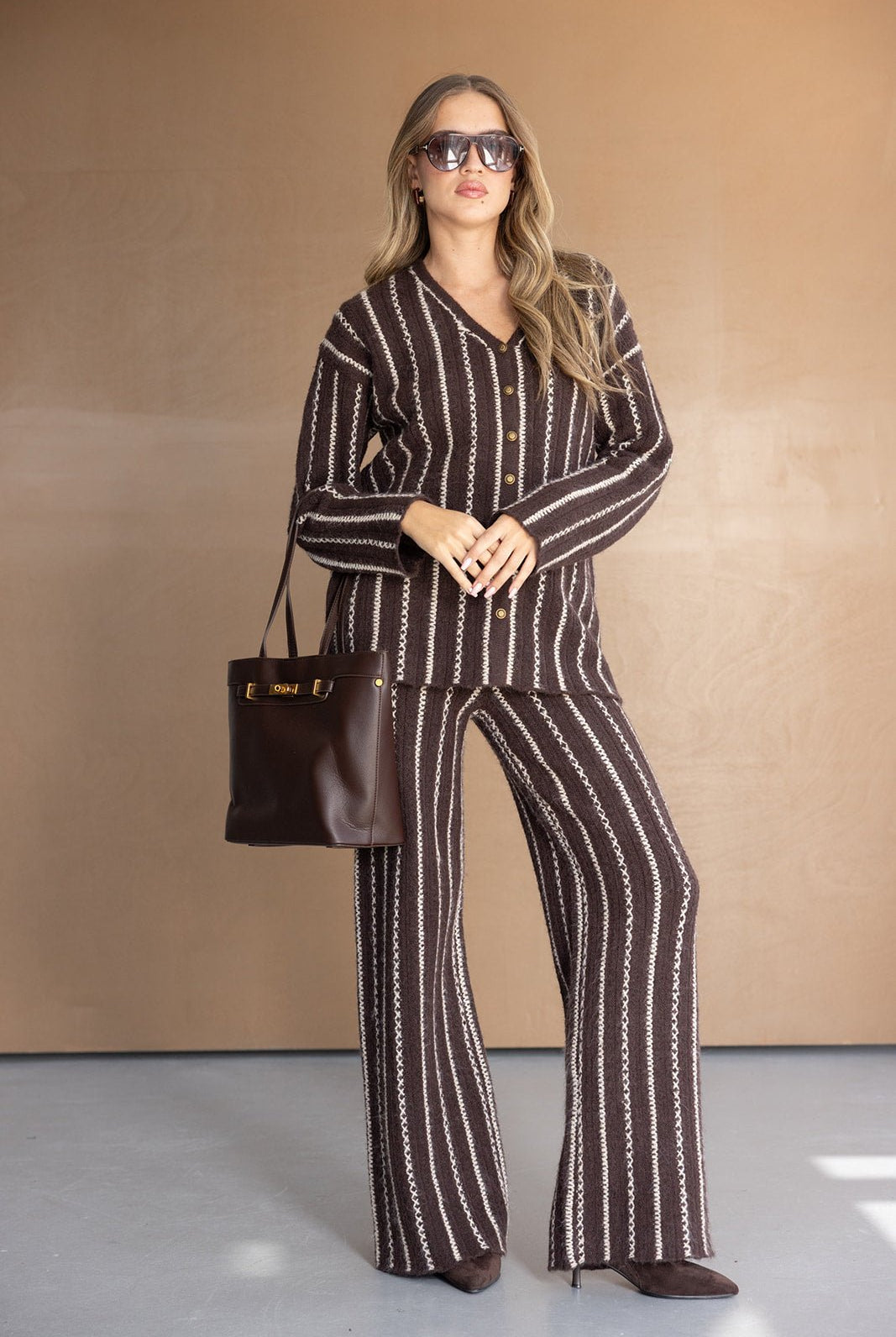 אישה לובשת חליפת נשים חומה מפוספסת, מחזיקה תיק חום ונועלת נעלי עקב, אופנת חורף