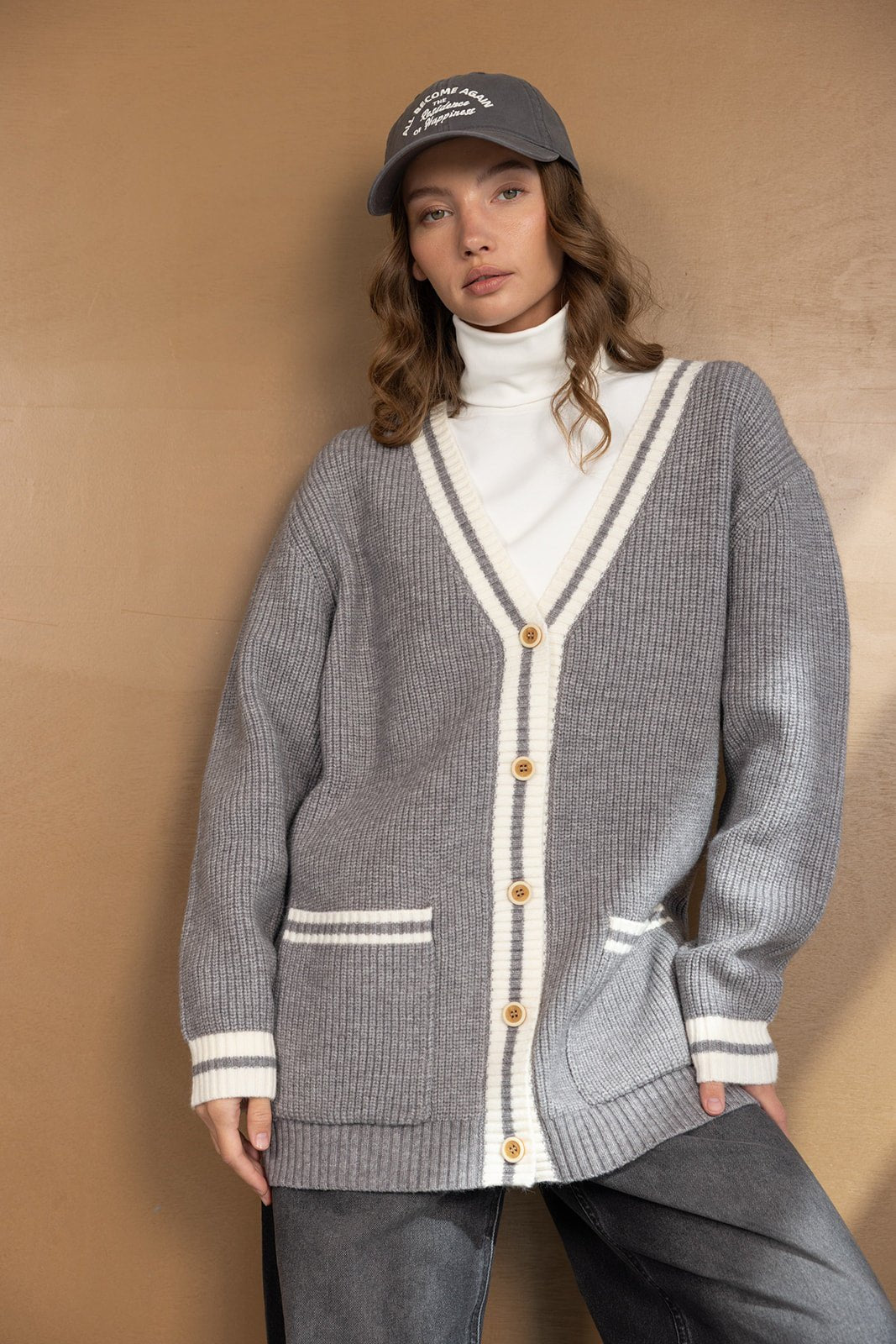 דוגמנית לובשת קרדיגן סרוג אפור עם כפתורים ומכנסי ג'ינס, חולצה לבנה וגזרה קז'ואל אופנתית