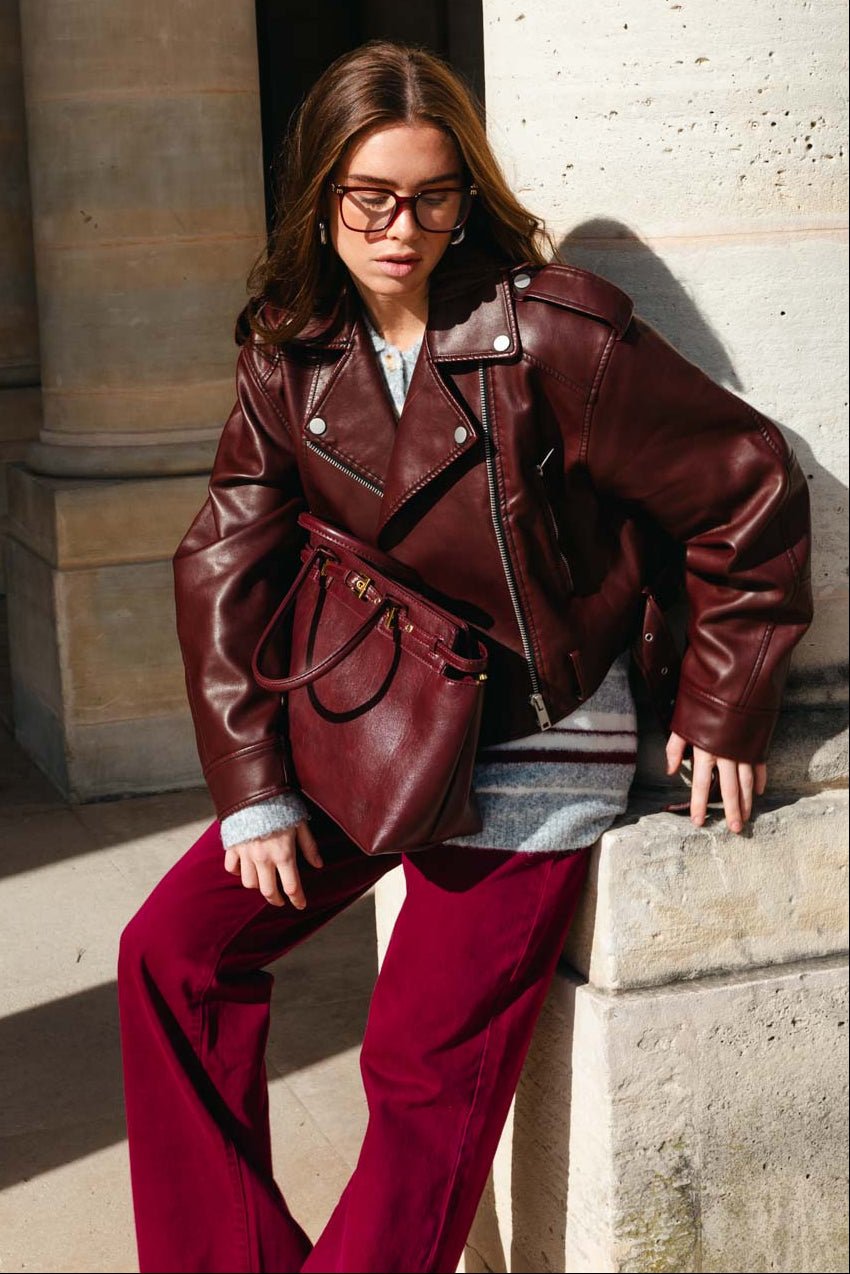 אישה עם מעיל עור בורדו, מכנסיים תואמים ותיק אופנתי, מראה אופנה לנשים צעירות