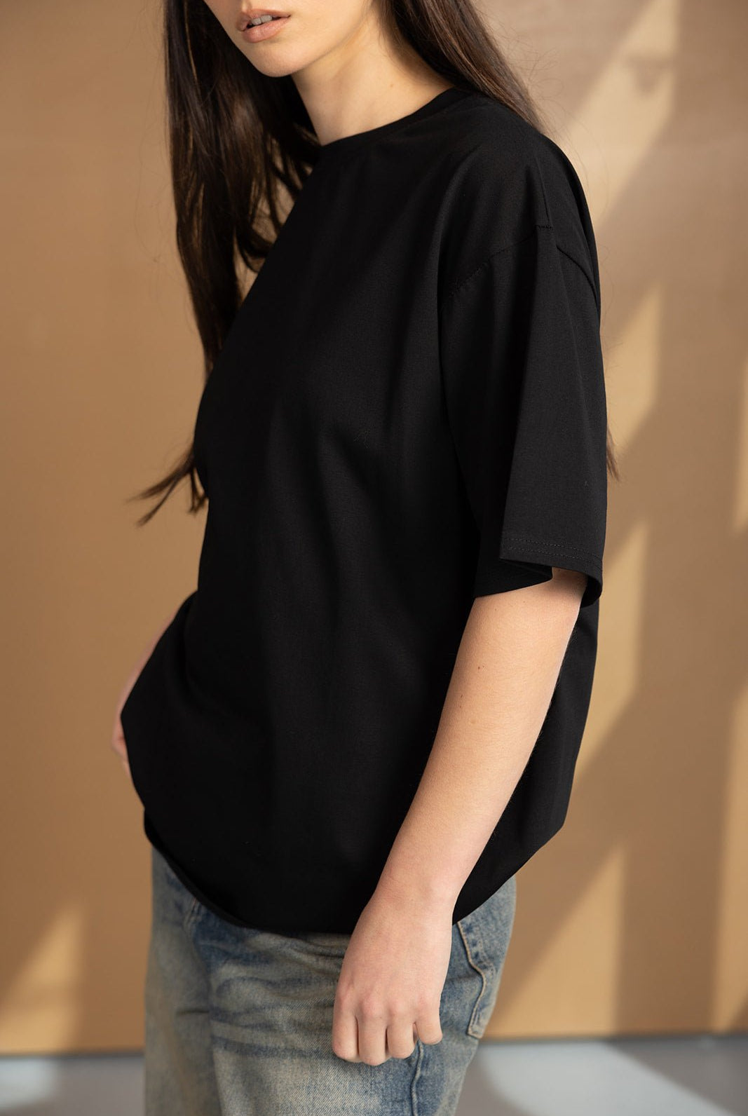 אישה עם שיער ארוך לובשת טי שירט שחורה וג'ינס אופנתי, אופנת נשים צעירה