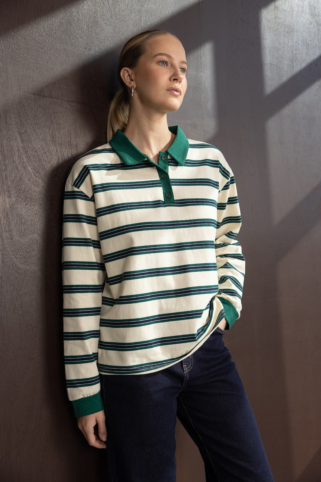 אישה לובשת חולצת פולו פסים ירוקה ולבנה עם שרוולים ארוכים ומכנסי ג'ינס אופנתיים