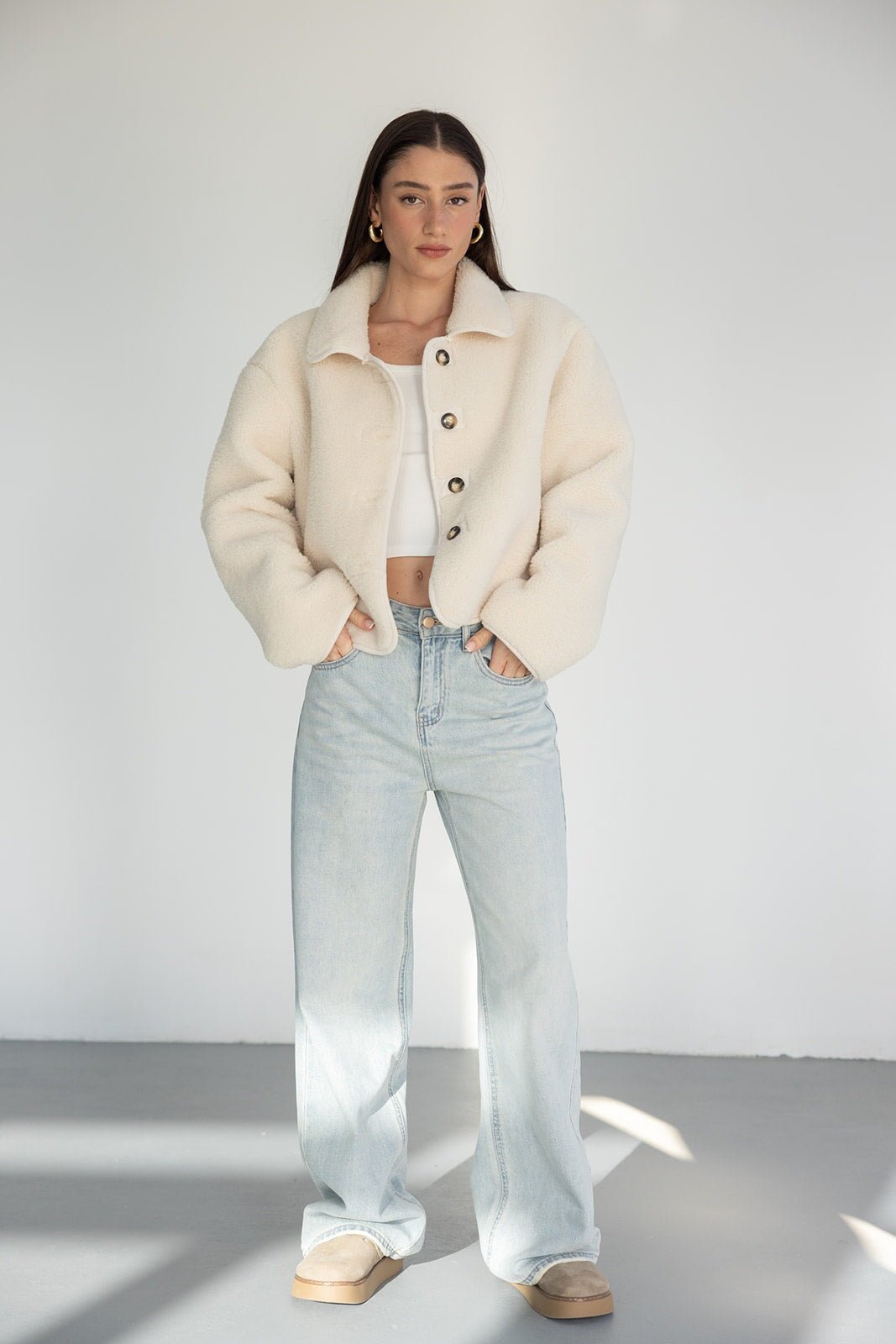 דוגמנית לובשת ג'קט בוקסה קרם עם כפתורים, ג'ינס בגזרה רחבה ונעליים בהירות, אופנת נשים עדכנית