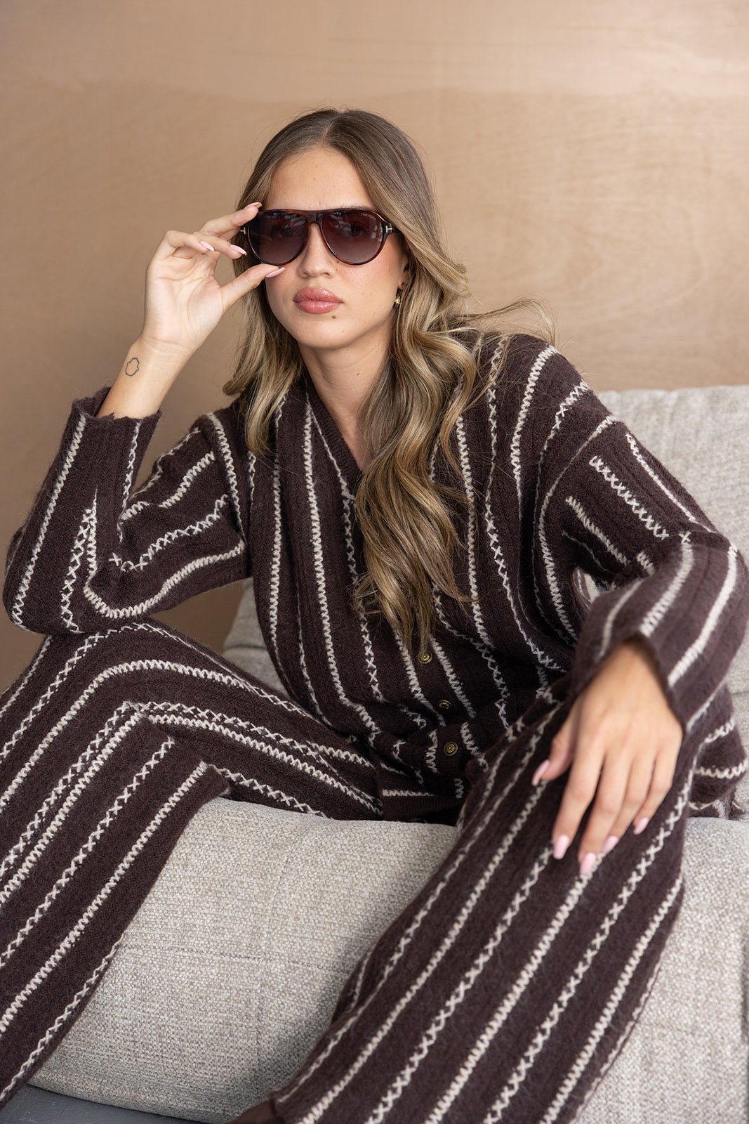 אישה יושבת לובשת סט פסים חום-קרם מחמם עם משקפי שמש, אופנת חורף לנשים