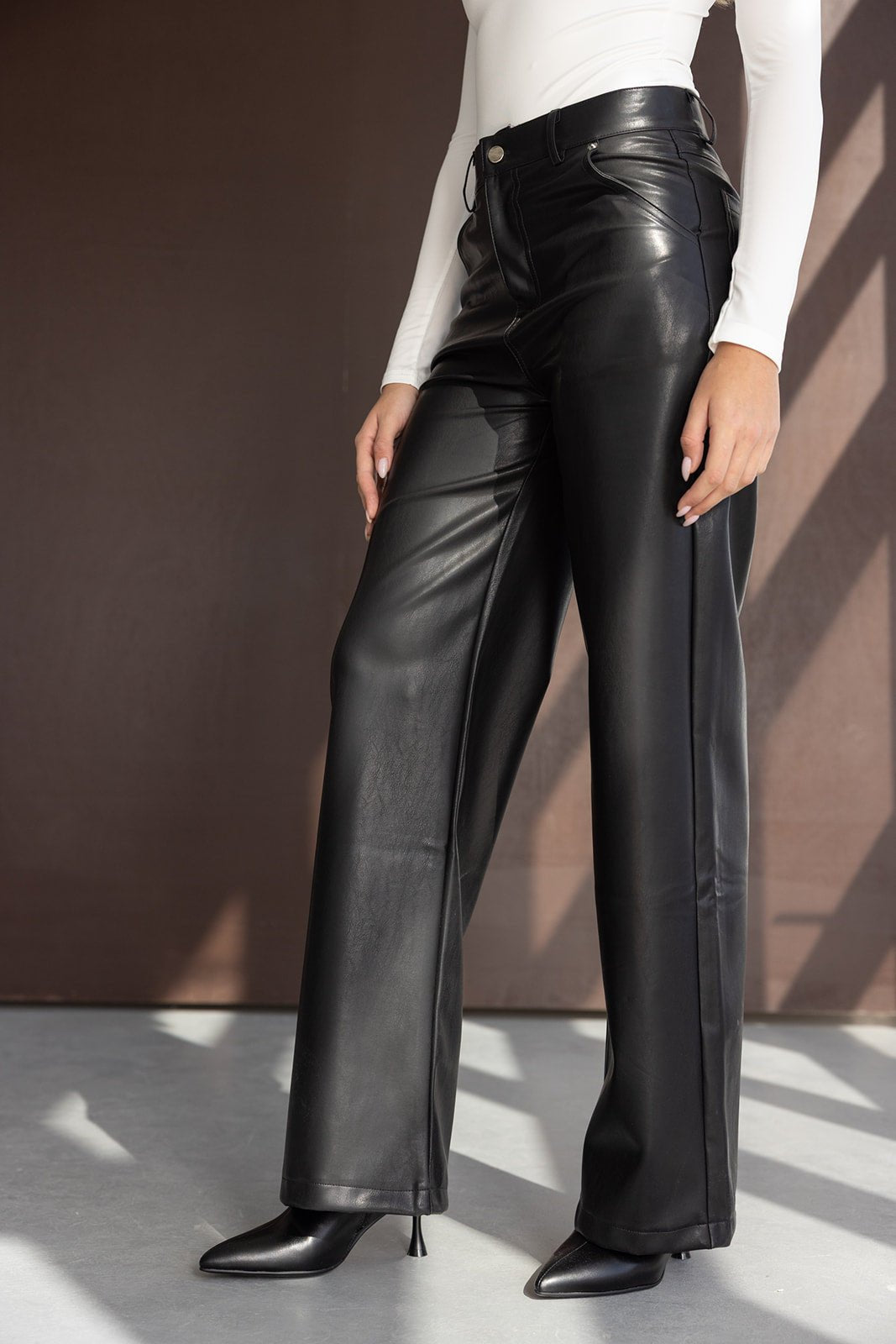 מכנסי דמוי עור שחורים לנשים בגזרה רחבה, עם חולצה לבנה ונעלי עקב אופנתיות