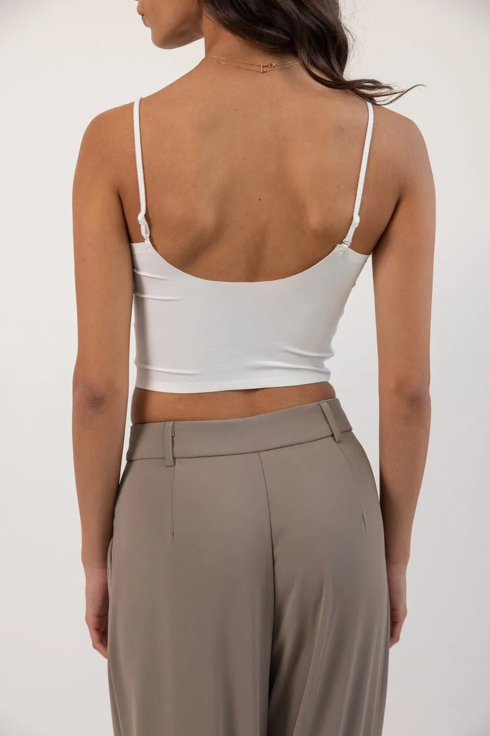 אישה לובשת טופ לבן דק עם כתפיות ומכנסיים מחויטים אפורים, צילום מאחור