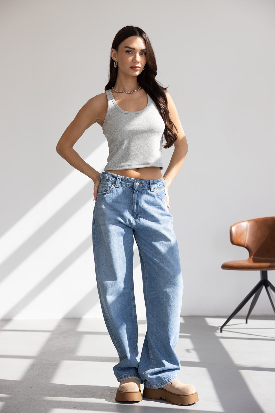 אישה לובשת גופיה אפורה ומכנסי ג'ינס רחבים אופנתיים, נעלי פלטפורמה בז', בסטודיו מואר