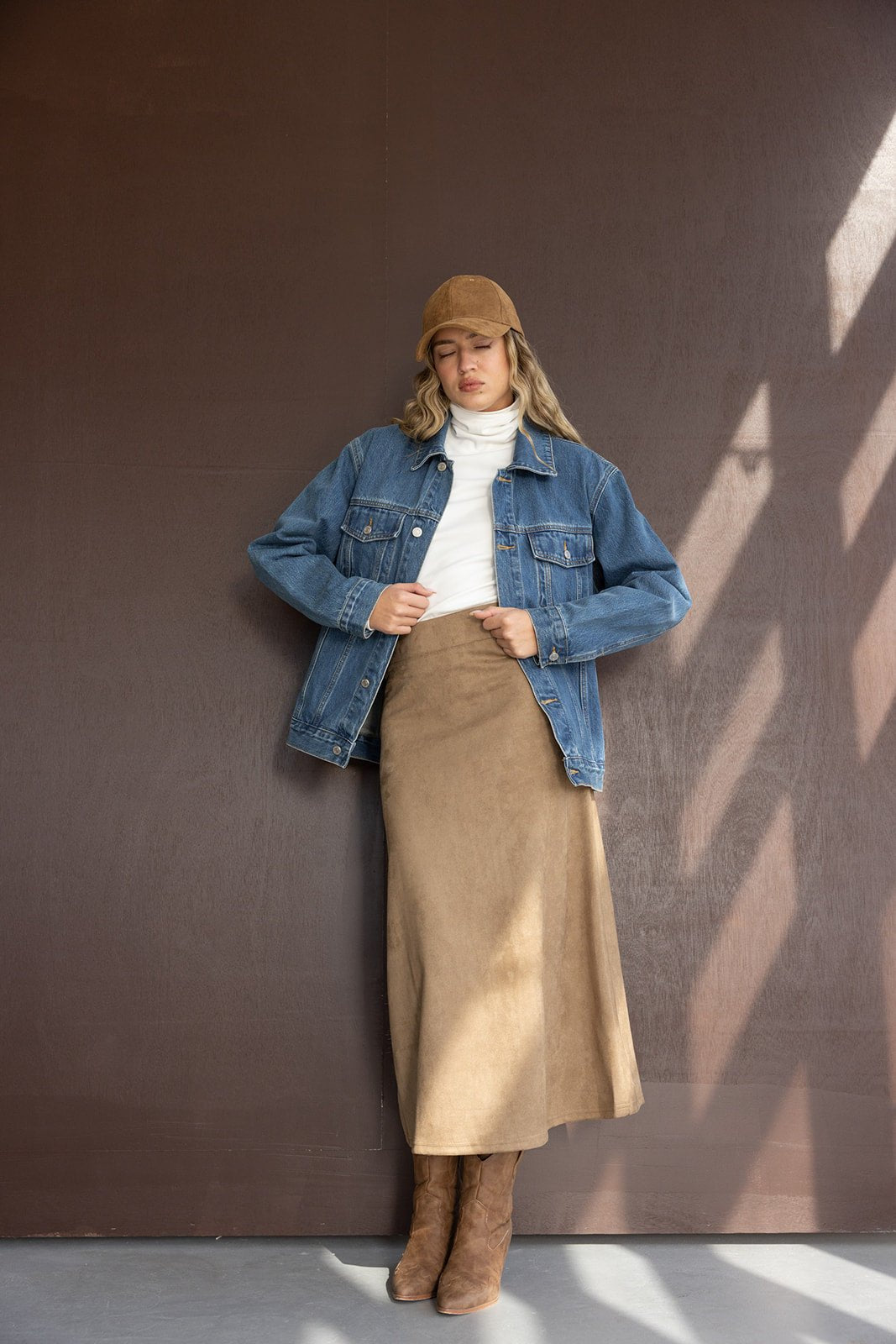 אישה עם ג'קט ג'ינס, חצאית וחולצה ארוכה, כובע ומגפיים בגווני חום, אופנה עדכנית לנשים