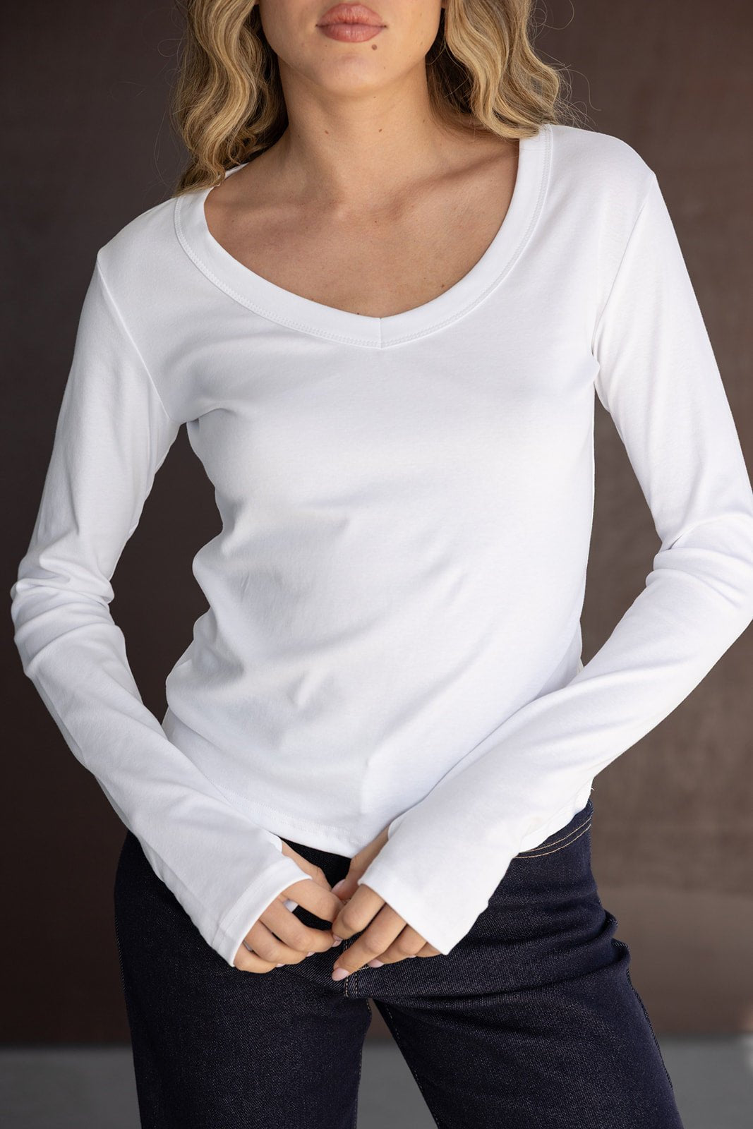 דוגמנית לובשת חולצת נשים לבנה עם שרוול ארוך ומכנסי ג'ינס, בגד אופנה לנערות