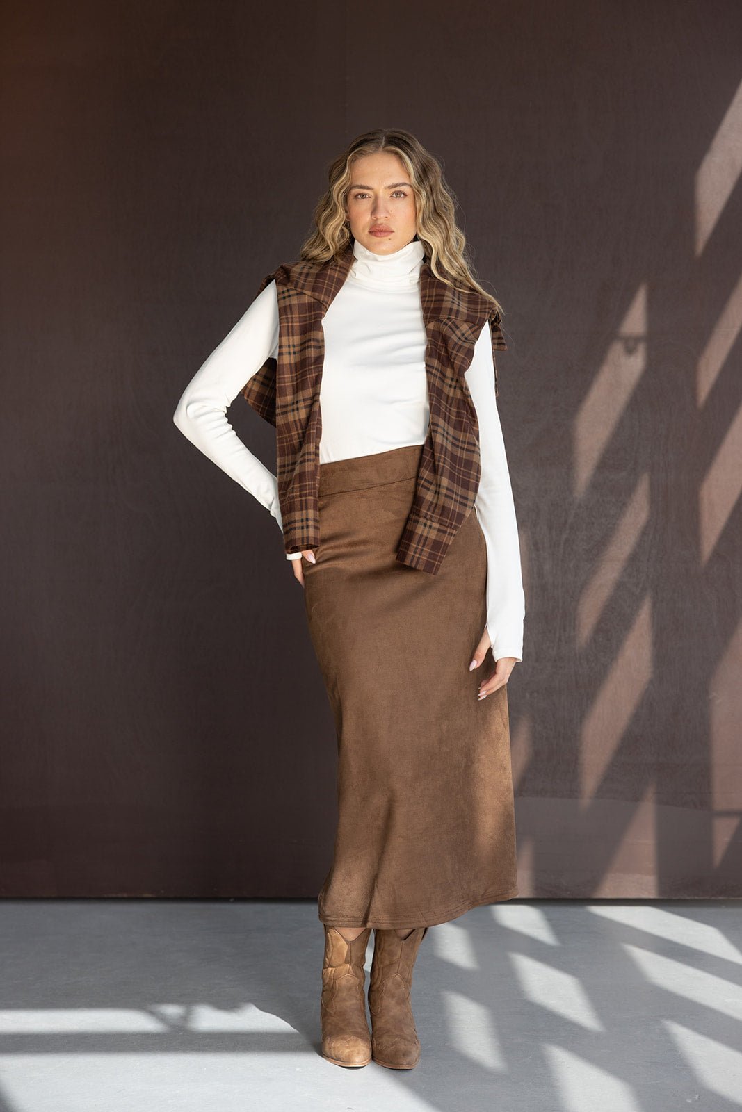 דוגמנית לובשת חצאית חומה, גולף לבן, חולצה משובצת חומה ומגפיים חומים, אופנה לנשים