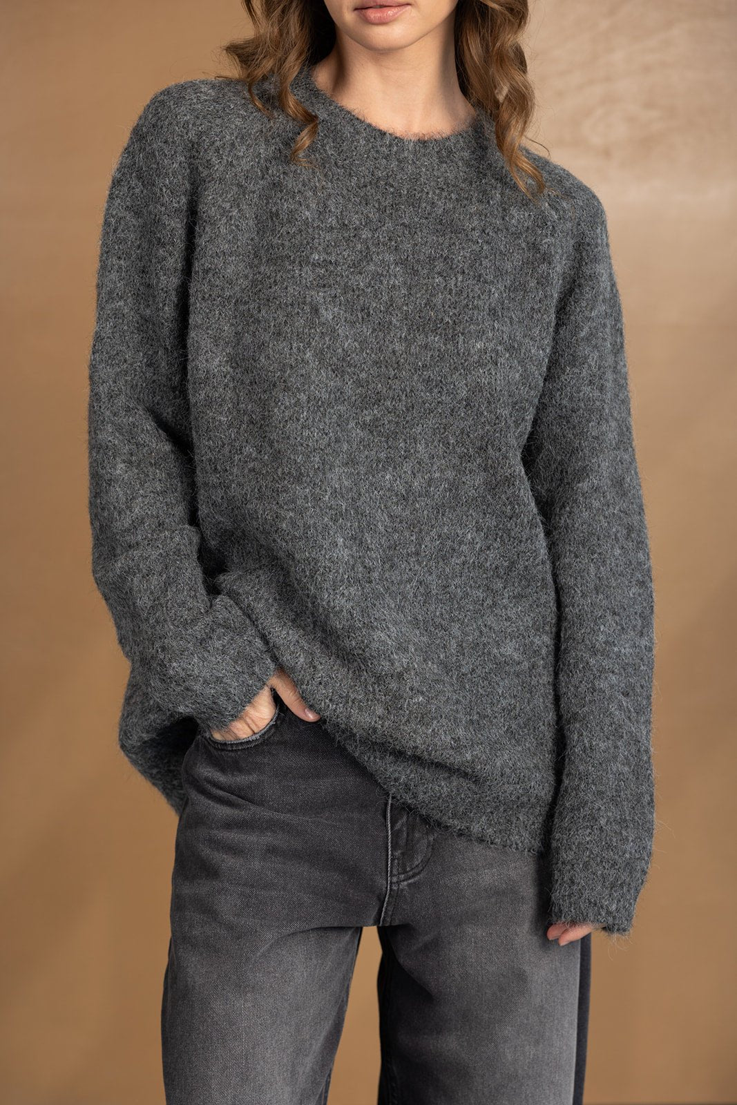 דוגמנית לובשת סוודר צמר אפור ומכנסי ג'ינס כהים, בגדי חורף לאופנה לנשים