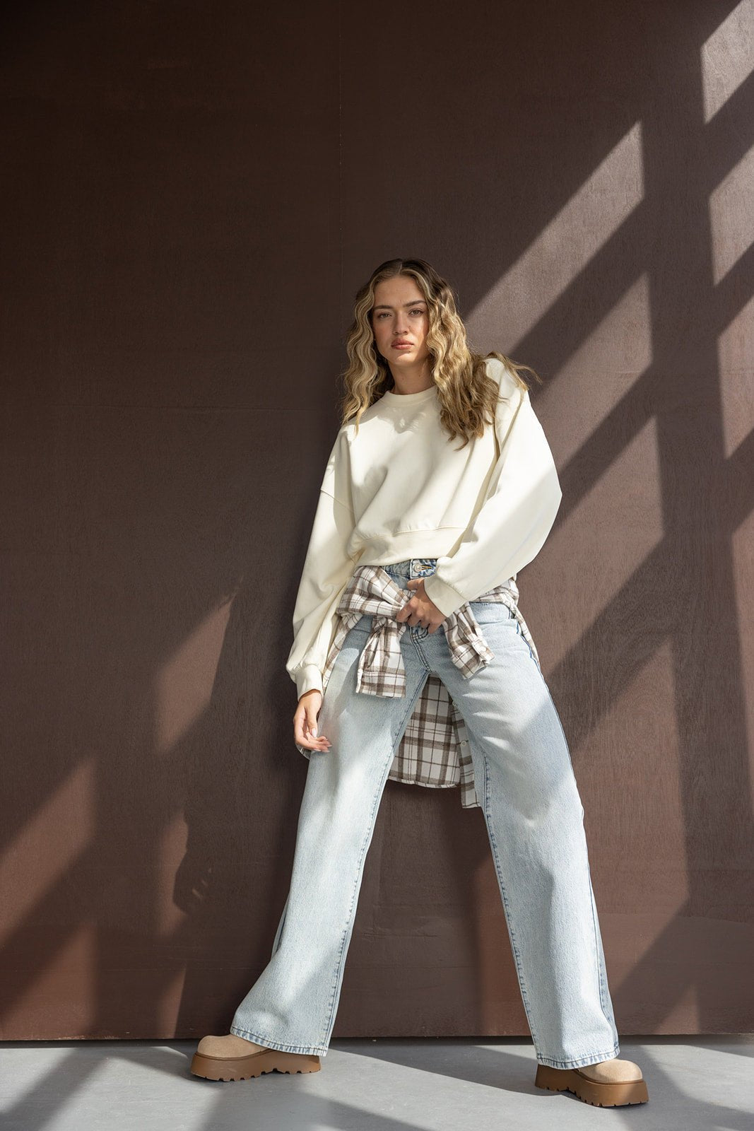 דוגמנית בלבוש אופנתי לנערות עם סווטשירט שמנת, ג'ינס רחב, חולצה משובצת קשורה ומגפיים טרנדיים