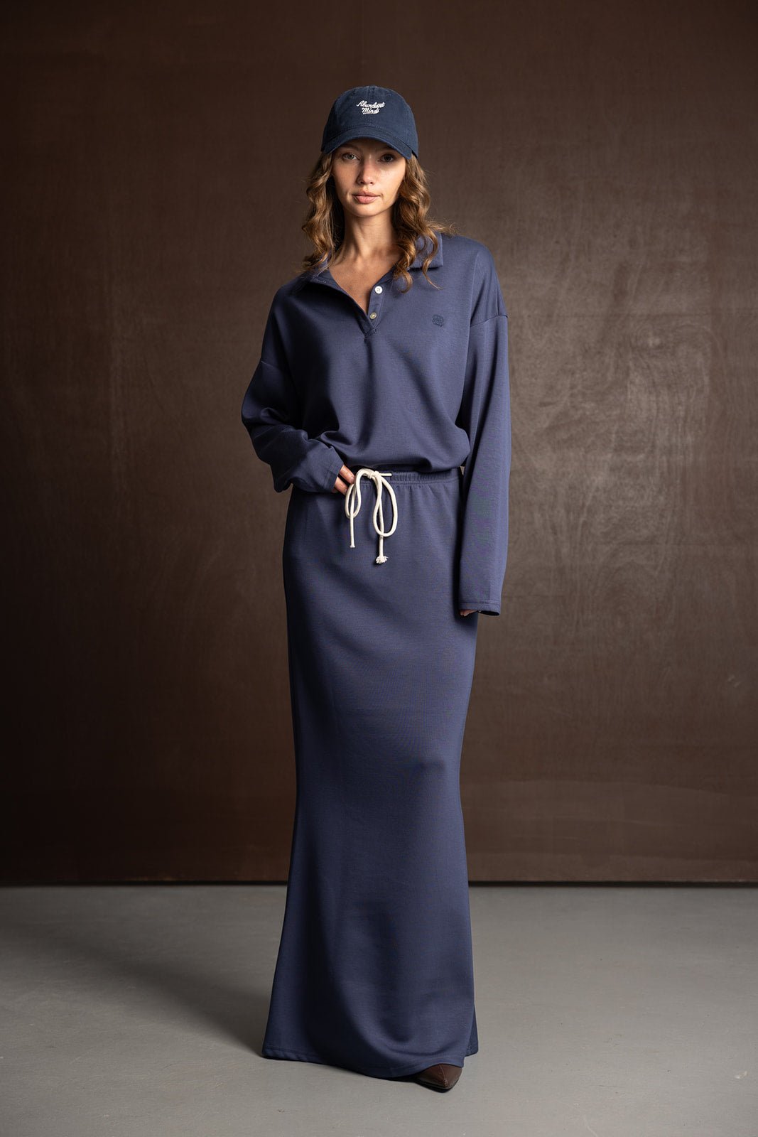 דוגמנית לובשת שמלת טרנינג כחולה בסגנון ספורט אלגנט עם שרוך, וכובע מצחייה תואם