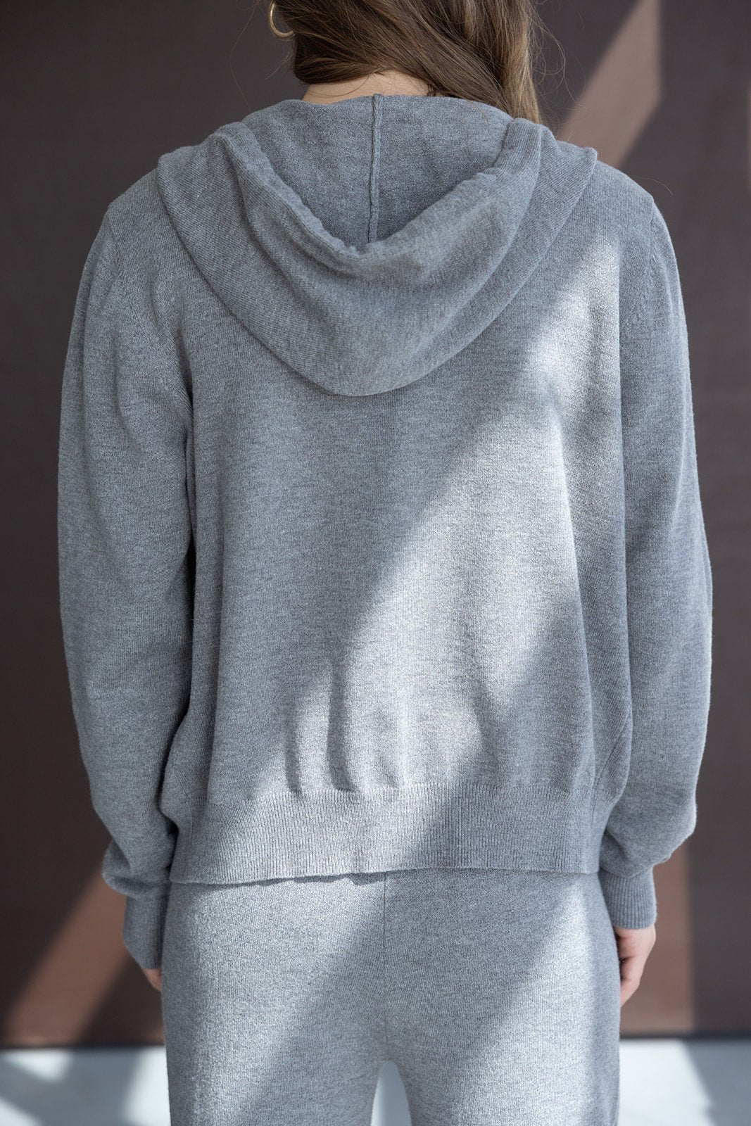 אישה עם סט טרנינג אפור לנשים, סריג עם קפוצ׳ון ומכנס תואם, מצולמת מאחור