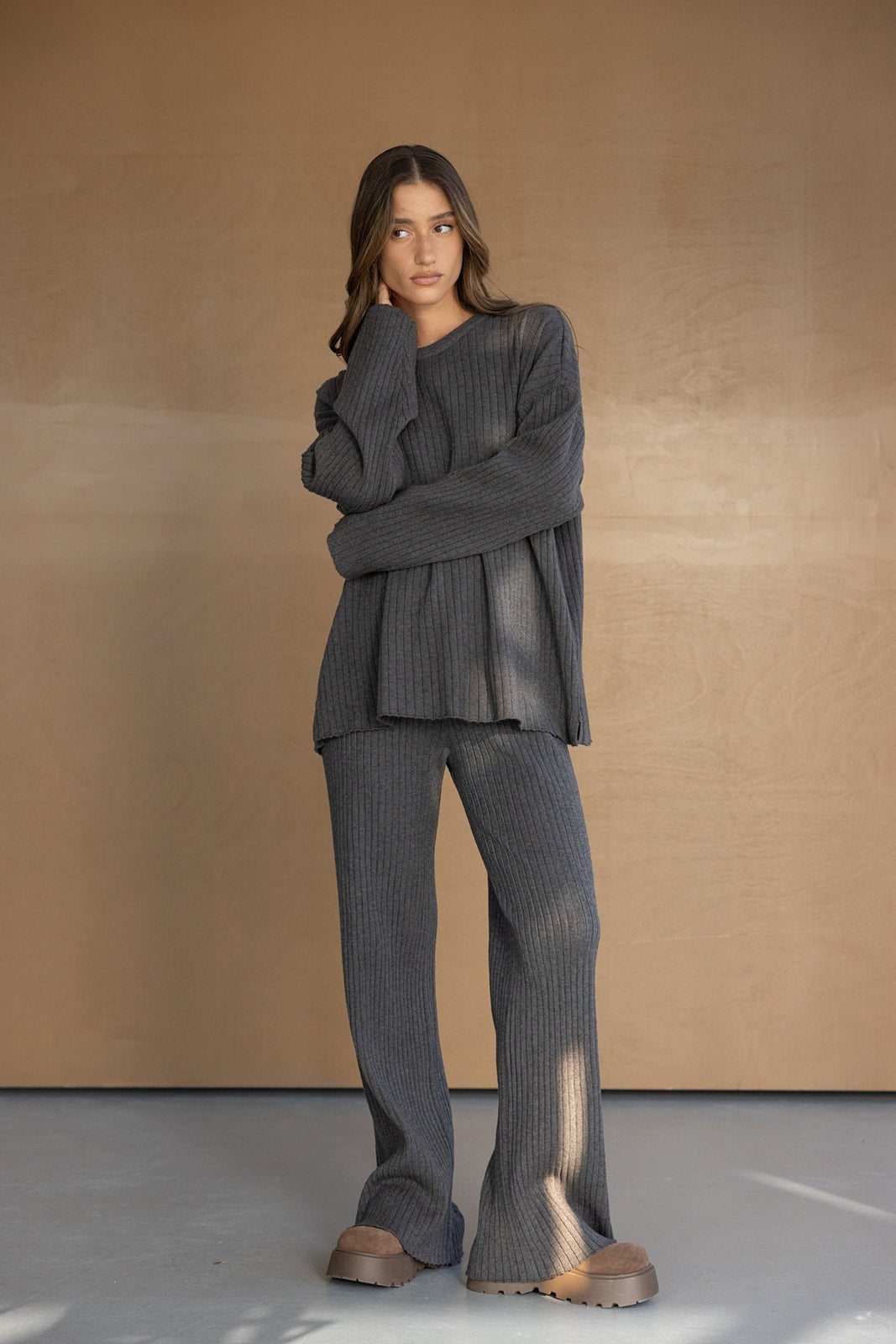 דוגמנית לובשת סט תואם מחמם בגוון אפור כהה, חולצה ומכנסיים מבד סריג בסגנון טרנדי, רקע נייטרלי