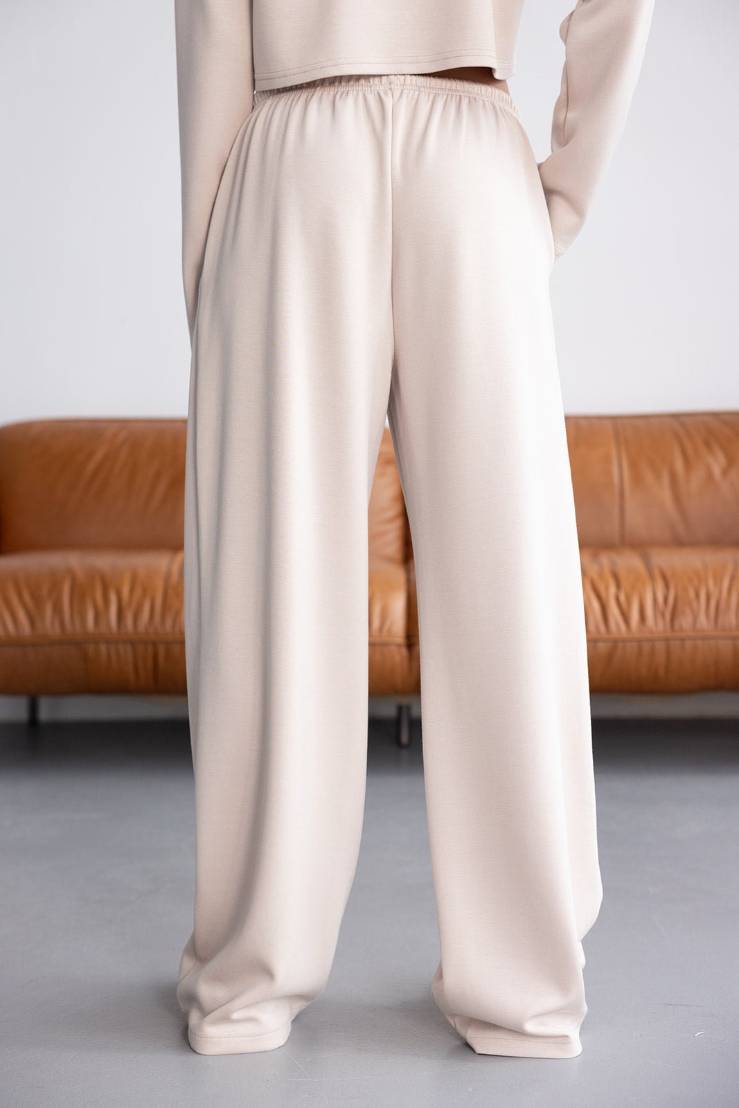 מכנסי נשים רחבים בגזרת טרנינג בצבע בז' בסגנון קז'ואל, רקע סלון מודרני.