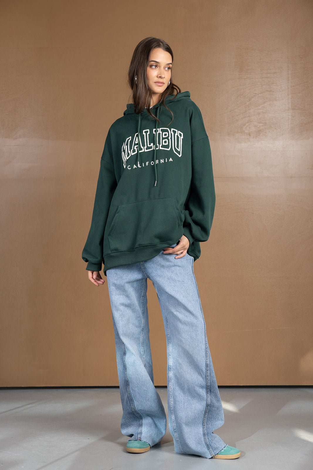 צעירה עם קפוצ׳ון ירוק MALIBU ומכנסי ג׳ינס בגזרה רחבה, אופנת רחוב לנשים