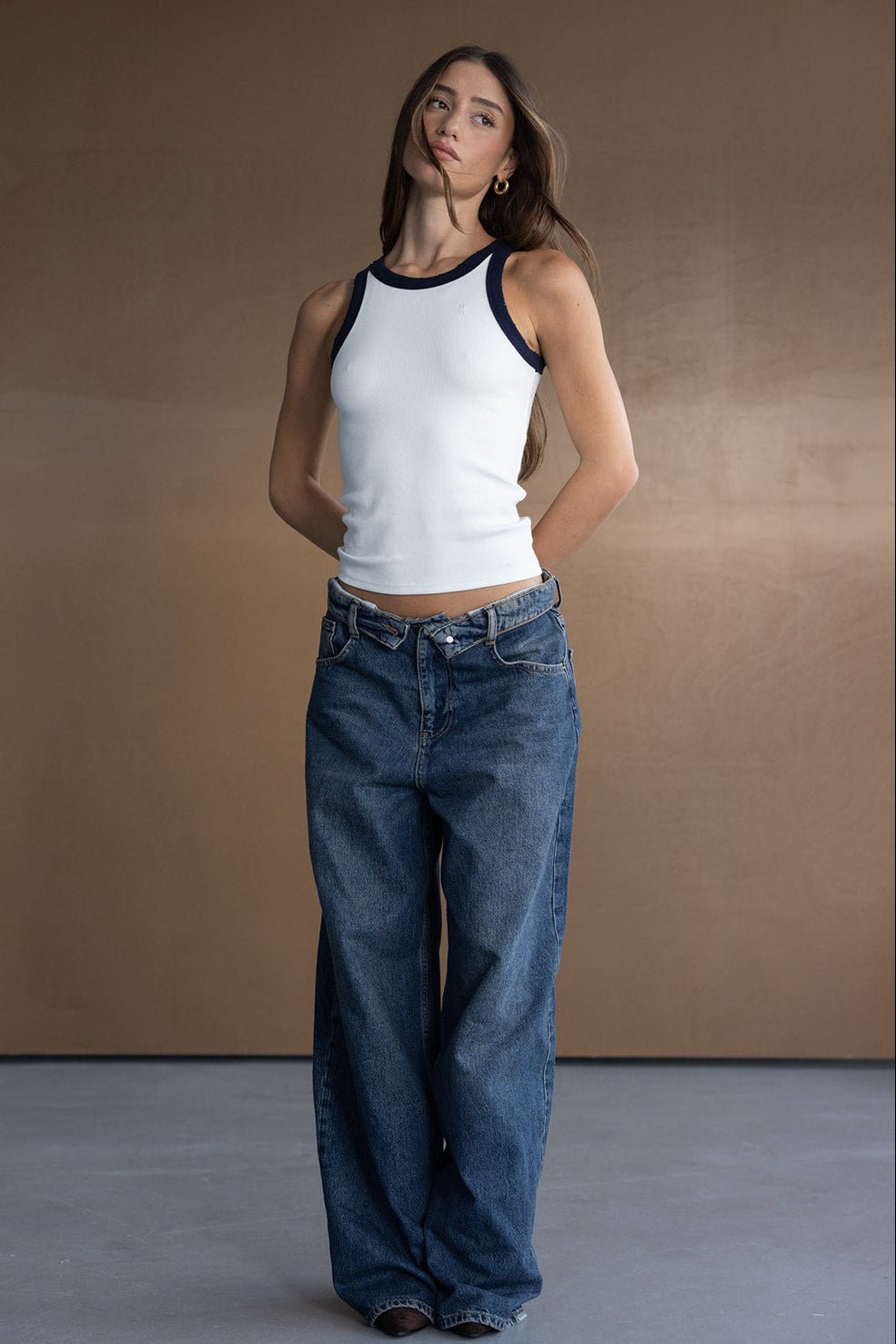 אישה צעירה לובשת ג׳ינס רחב בגזרה גבוהה וגופיית ספורט לבנה עם שוליים כהים, אופנת נשים טרנדי