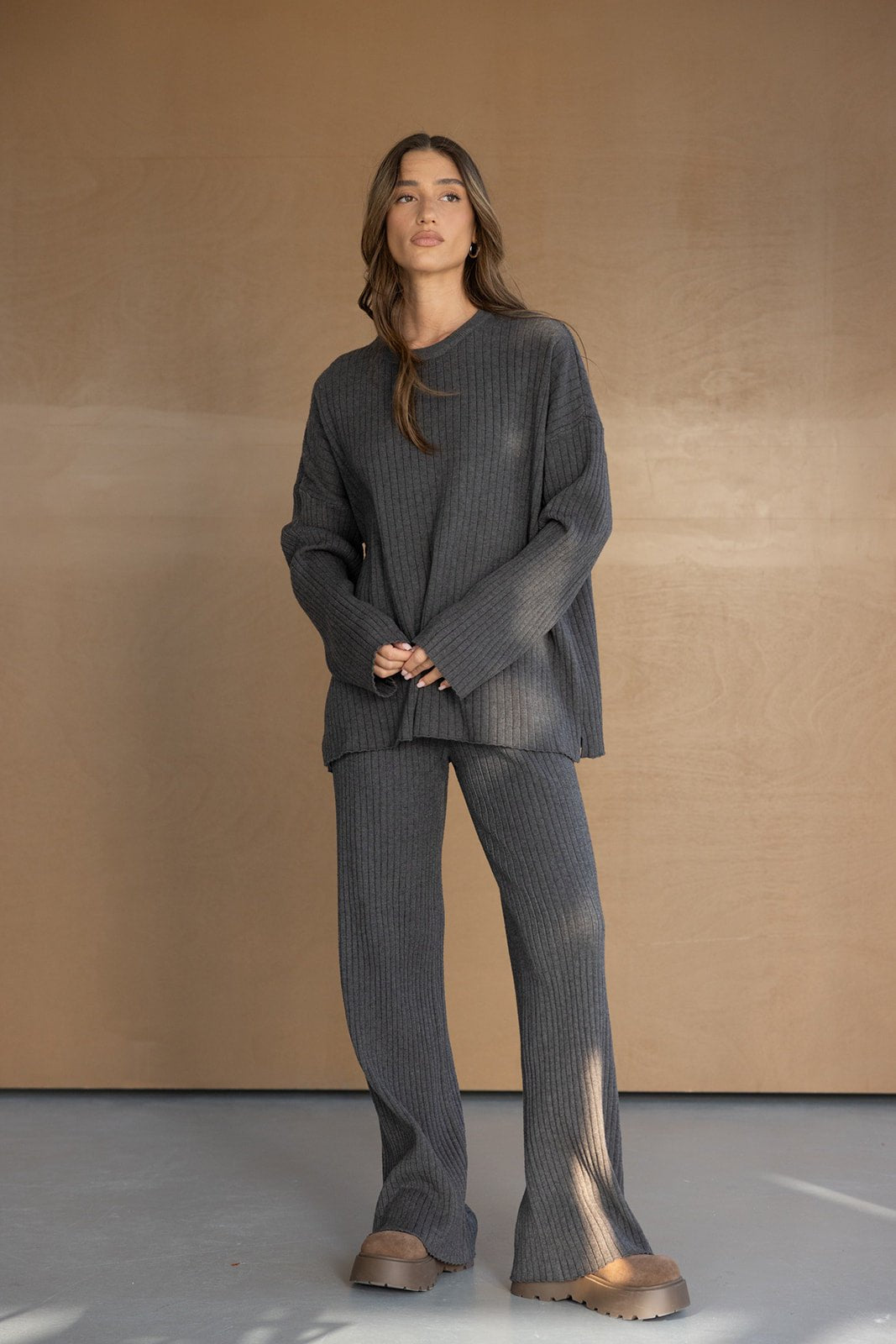 אישה לובשת סט סריגים אפור כהה מחמיא, חולצה ארוכה ומכנסיים רחבים, אופנת חורף לנשים