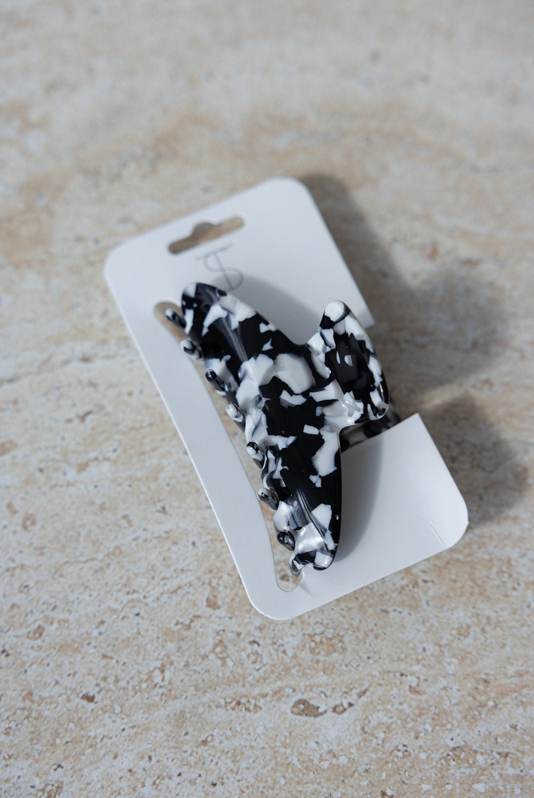 קליפס שיער טרנדי שחור עם דוגמת שיש לבנה, מונח על כרטיס קרטון לבן, לאביזרי שיער אופנתיים