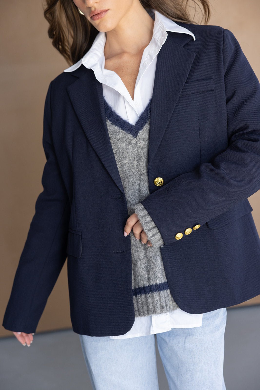 אישה עם בלייזר כחול קלאסי, סוודר אפור, חולצה לבנה ומכנסי ג'ינס אופנתיים