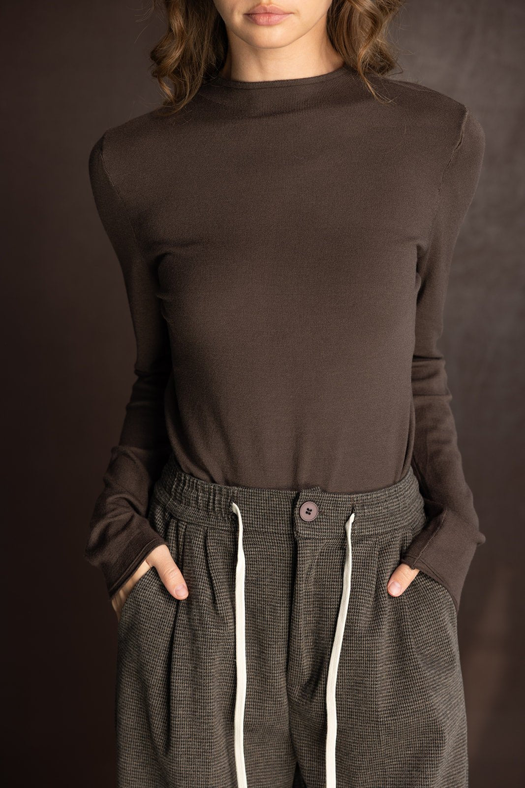 אישה לובשת חולצה חומה עם שרוולים ארוכים ומכנסיים משובצים בגזרה רחבה, אופנת נשים עדכנית