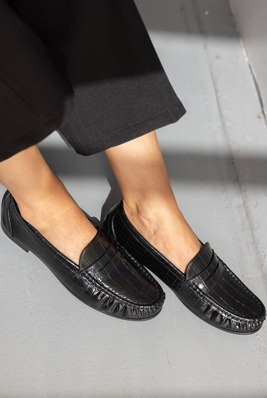 נעליים שטוחות לנשים בטקסטורת עור שחור, סטייל אופנתי על רקע רצפת בטון