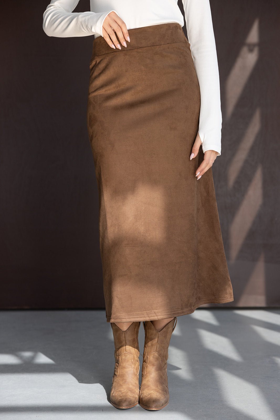 חצאית חום מידי בטקסטורת זמש לאישה עם חולצה לבנה ומגפיים חומים, אופנת נשים צעירה