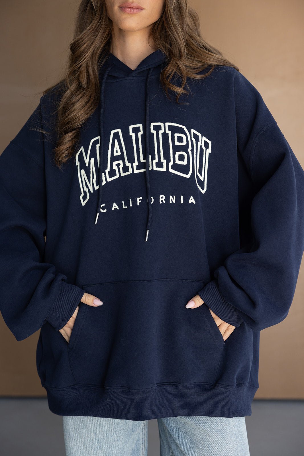 אישה לובשת קפוצ'ון כחול כהה עם כיתוב MALIBU CALIFORNIA, אופנת נשים חורפית טרנדית