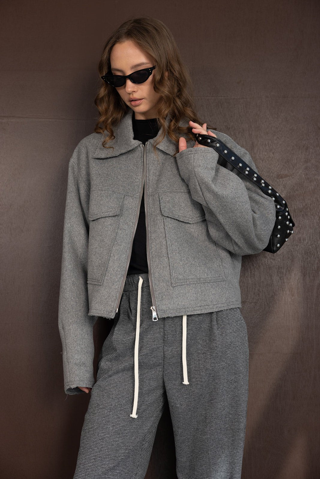 אופנת נשים, דוגמנית עם ג'קט אפור, מכנסיים מחויטים, משקפי שמש ואביזר שחור, לוק חורפי וטרנדי