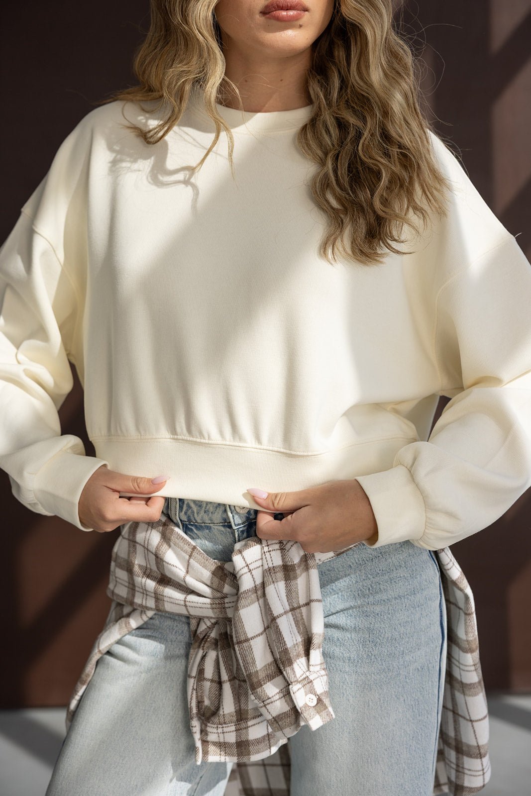 אישה לובשת סווטשירט שמנת אופנתי עם חולצה משובצת קשורה לג'ינס בהיר, אופנת נשים לשעות היום