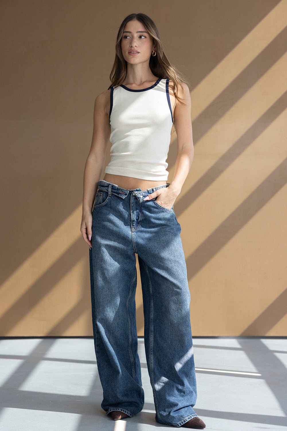 דוגמנית לובשת גופיית סריג לבנה עם קצוות כהים ומכנסי ג'ינס רחבים, אופנת נשים צעירה