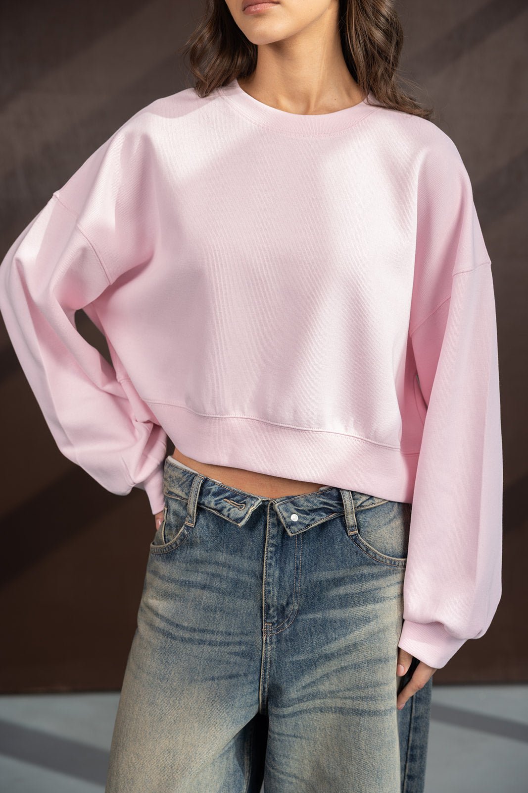 אישה לובשת סווצ'ר ורוד קצר עם שרוולים רחבים וג'ינס גבוה, אופנת נשים צעירה