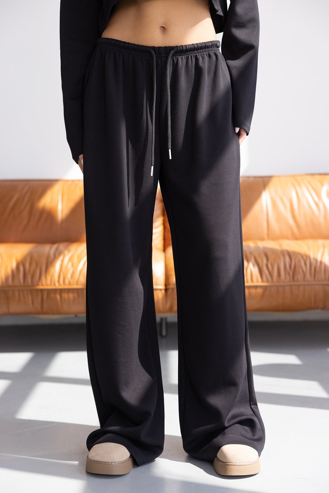 מכנסיים רחבים שחורים לנשים עם שרוך במותן, אופנת רחוב, צילום באור טבעי ליד ספה